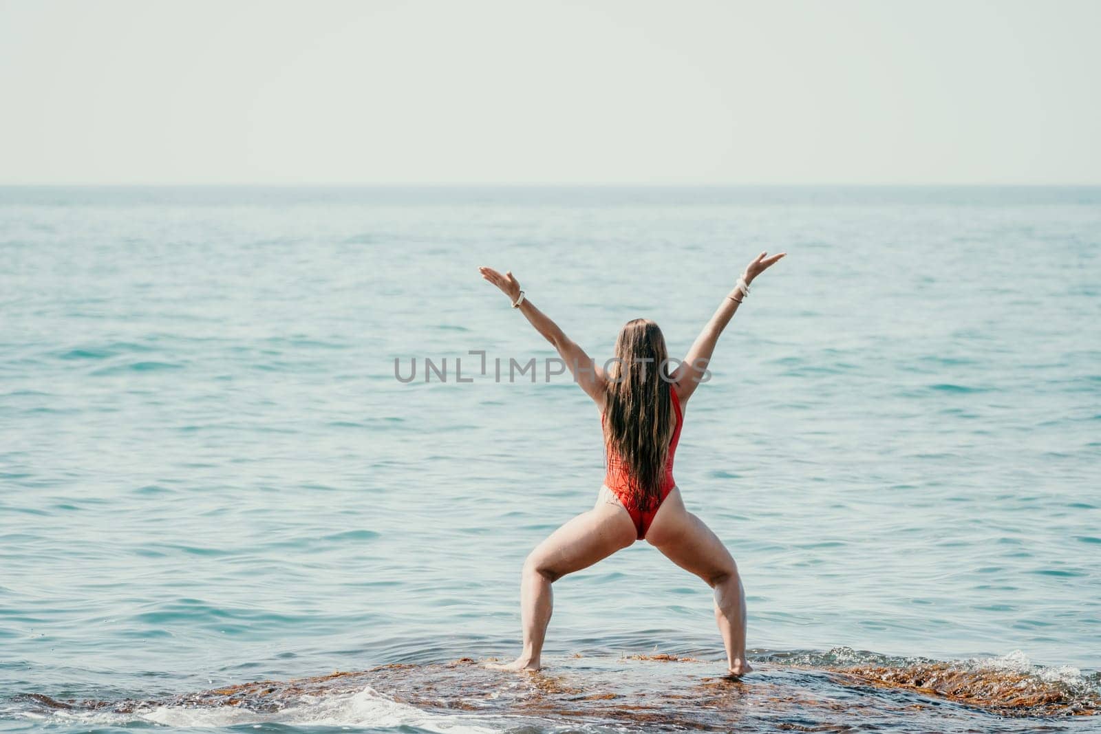 Woman sea yoga. Back view of free calm happy satisfied woman with long hair standing on top rock with yoga position against of sky by the sea. Healthy lifestyle outdoors in nature, fitness concept.