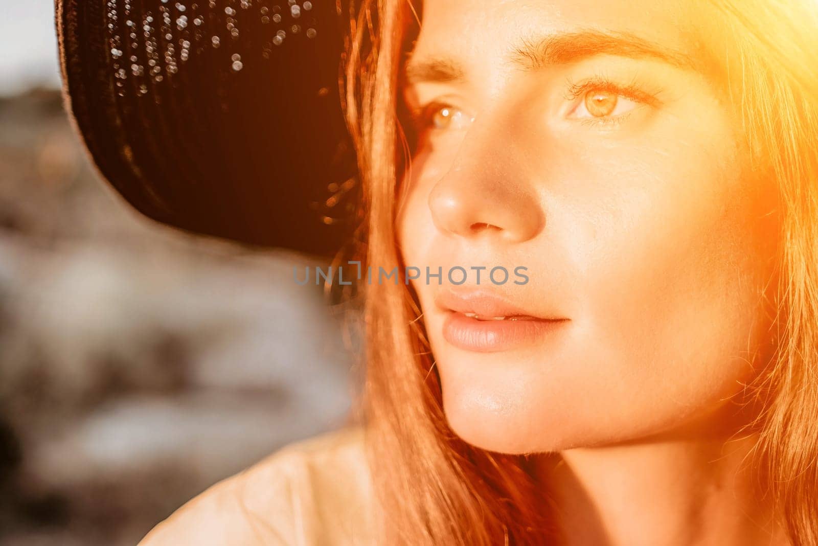 Portrait of happy young woman wearing summer black hat with large brim at beach on sunset. Closeup face of attractive girl with black straw hat. Happy young woman smiling and looking at camera at sea. by panophotograph