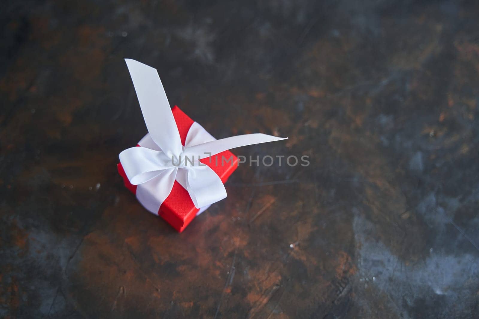 Small red gift box with a white bow on dark background. High-quality photo. Copy space.