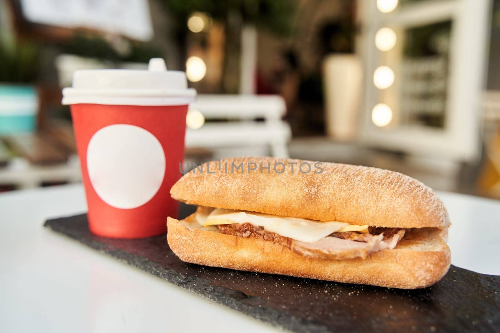 A sandwich with a red plastic glass of coffee on the table in a coffee shop. High-quality photo. Close-up