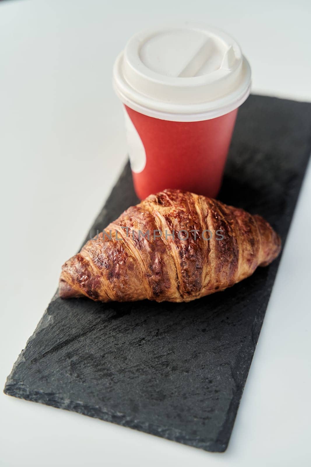 Red cup with coffee and a croissant on a table in a cafe. by driver-s