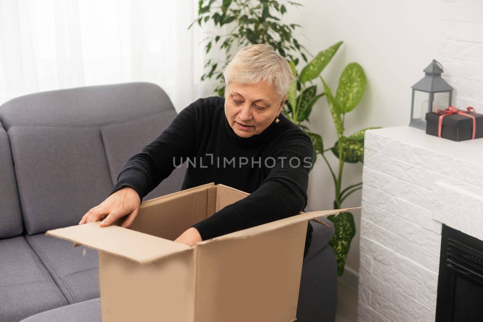 Elderly woman unpacking things in new house. Female hands opening cardboard box. Real estate, purchase, moving concept. by Andelov13