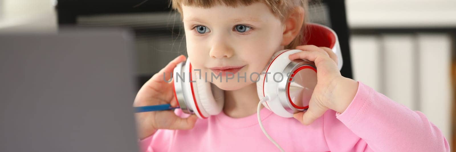 Beautiful little baby girl in headphones with laptop. Children educational videos and gadget addiction