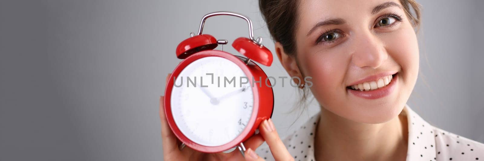 Portrait of beautiful smiling young woman holding alarm clock for ten o'clock by kuprevich