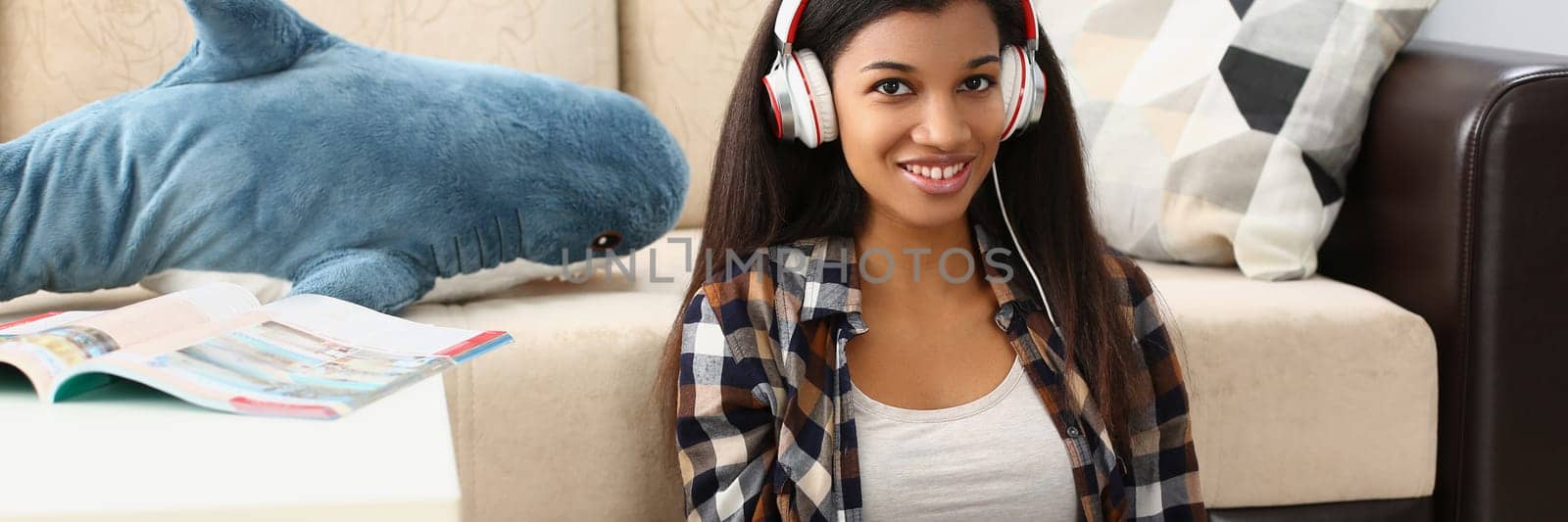 Young beautiful african american woman relaxing and listening to music with headphones on floor. Freelancer working remotely sitting at home with laptop concept