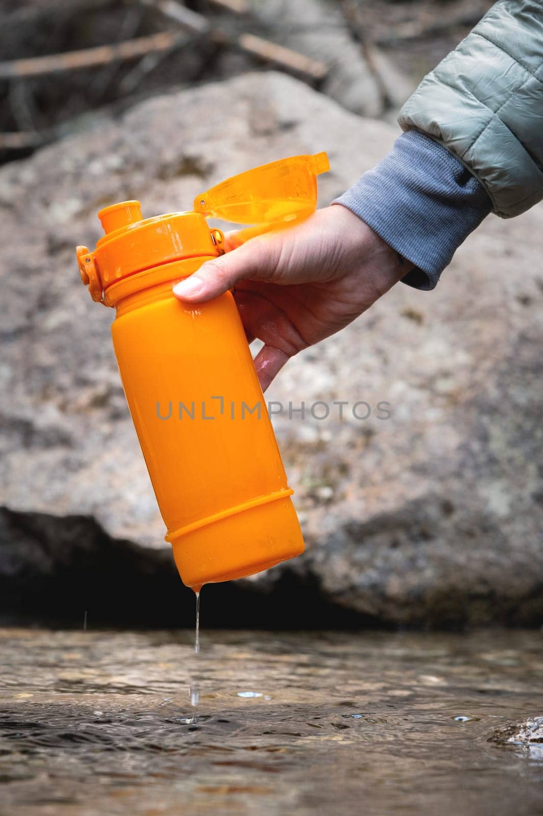Close-up of female hands filling fresh cold water into a silicone eco travel bottle during a water break on a tourist walking trail. The concept of active people or water resources, environmental friendliness of use.