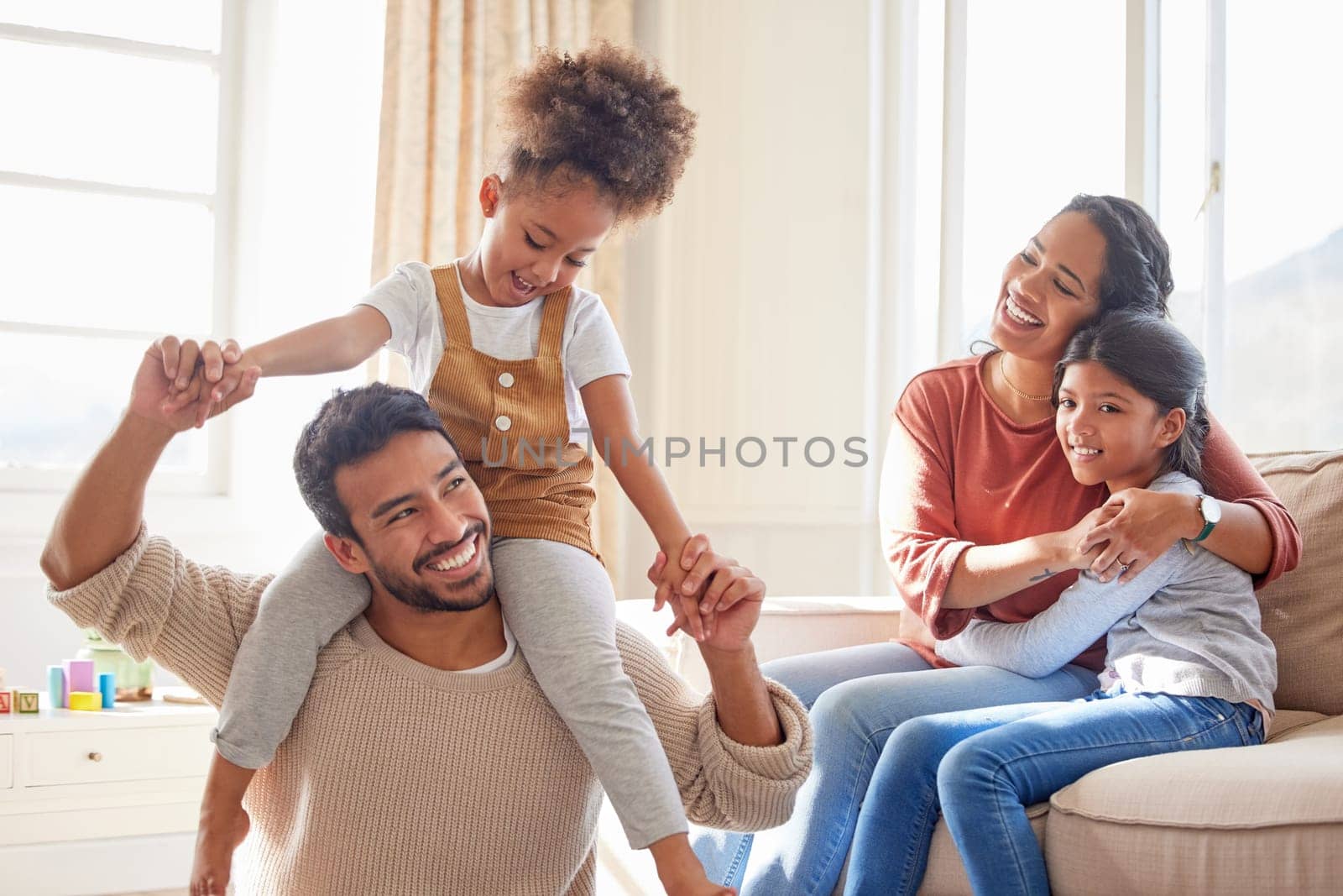 Dad, mom and children in home, shoulders and happiness with playing games, hug or bonding in lounge. Father, mother and daughter with care, love and together with embrace, quality time or living room.