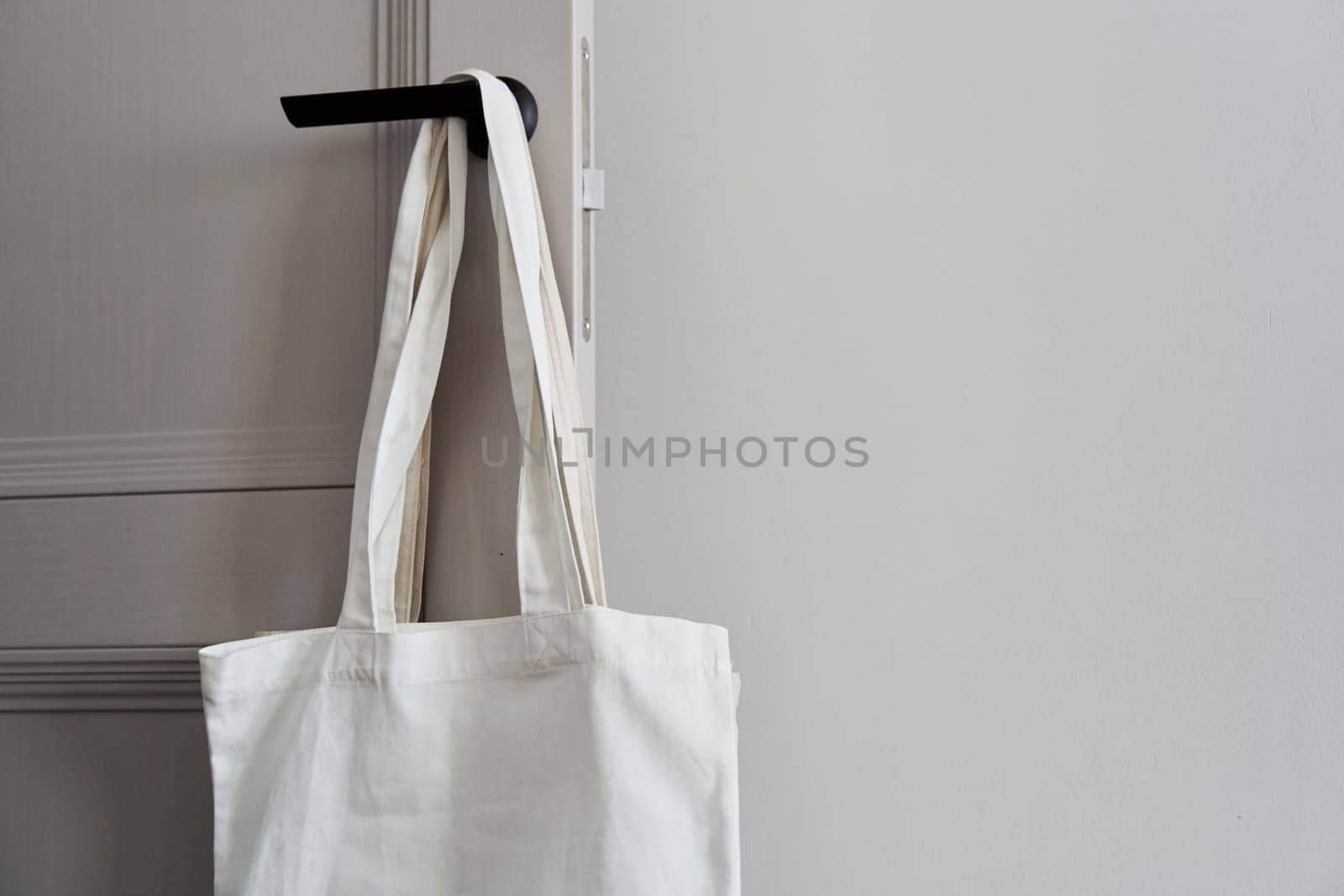 Eco friendly concept with white canvas tote bag hanging on door knob with two toned colored, Eco blank shopping sack with free copy space, Reduce plastic bags to reduce global warming. Canvas tote bag