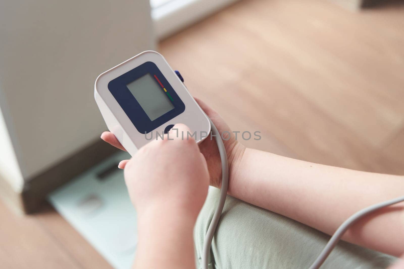 Selective focus girl is taking care for health with hearth beat monitor and blood pressure and heart rate monitor with digital pressure gauge. Health care and Medical concept. The topic of high blood pressure is hypertension disease. Close-up macro young caucasian woman hands using automatic tonometer to check pressure at home in bedroom on bed.