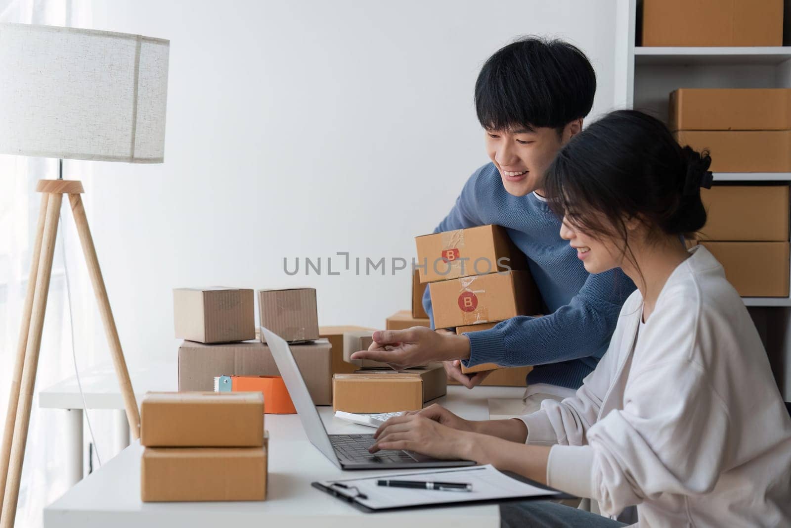 Couple of asian teenager owner business people work at home for online shopping, checking the order of product in technology computer and laptop, entrepreneur and life style concept.