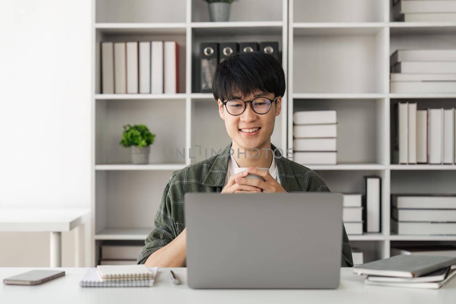 Asian handsome man working with laptop computer and drink coffee in living room happy and smile face.