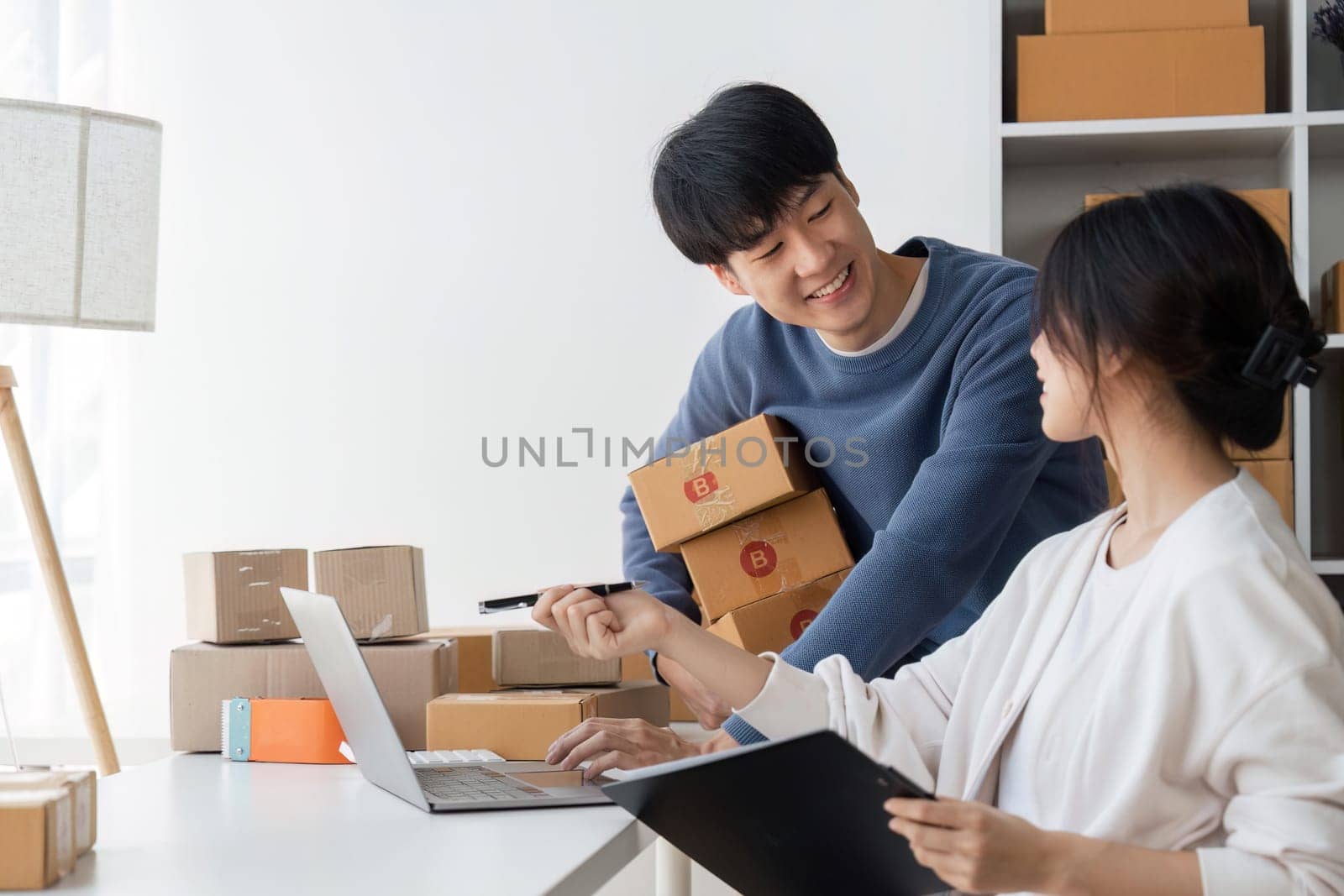 Couple startup small business working with laptop at workplace. freelance man and woman seller check product order, packing goods for delivery to customer. Online selling, e-commerce.