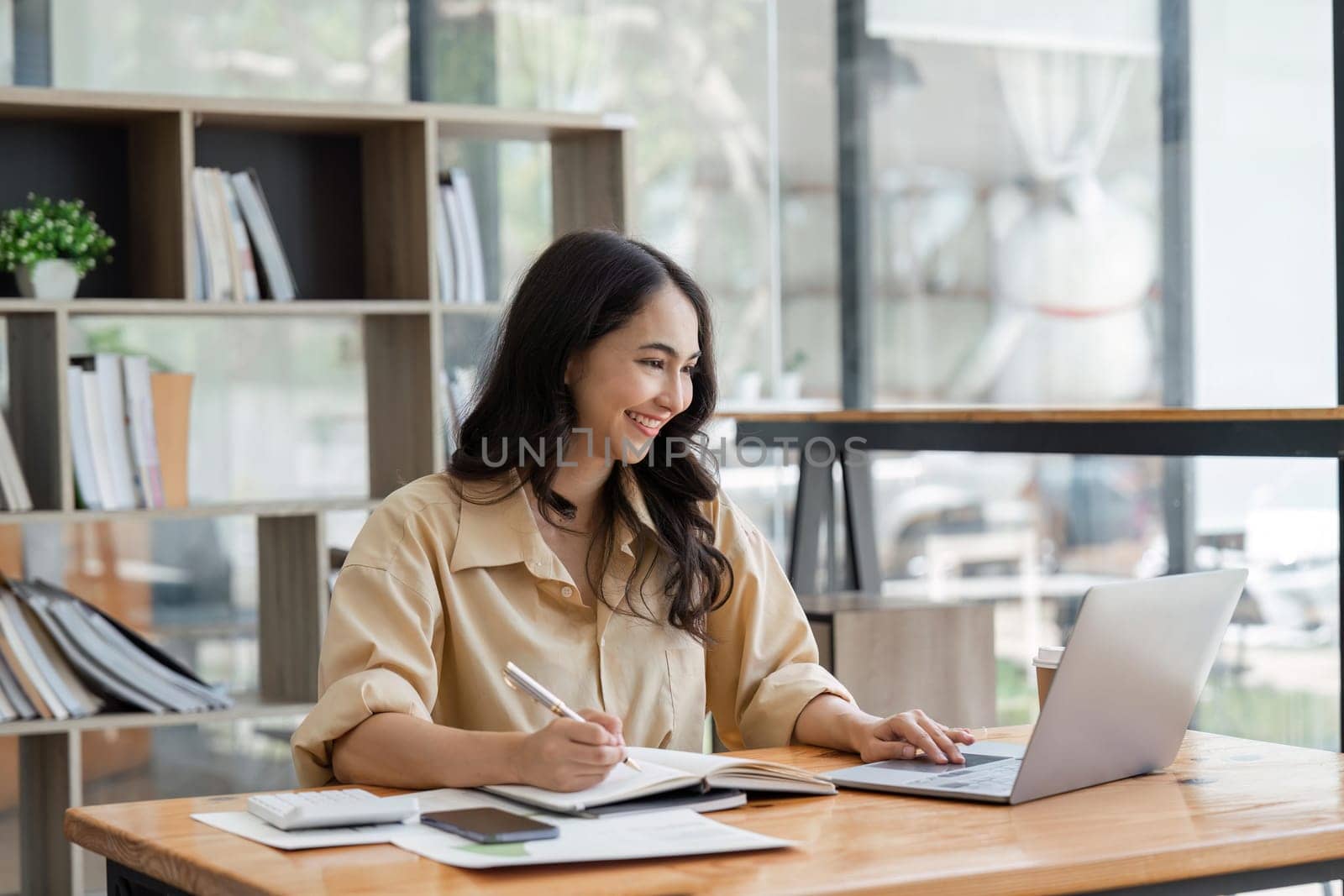 Portrait of beautiful smiling young businesswoman sitting at office bright modern work and typing on laptop.