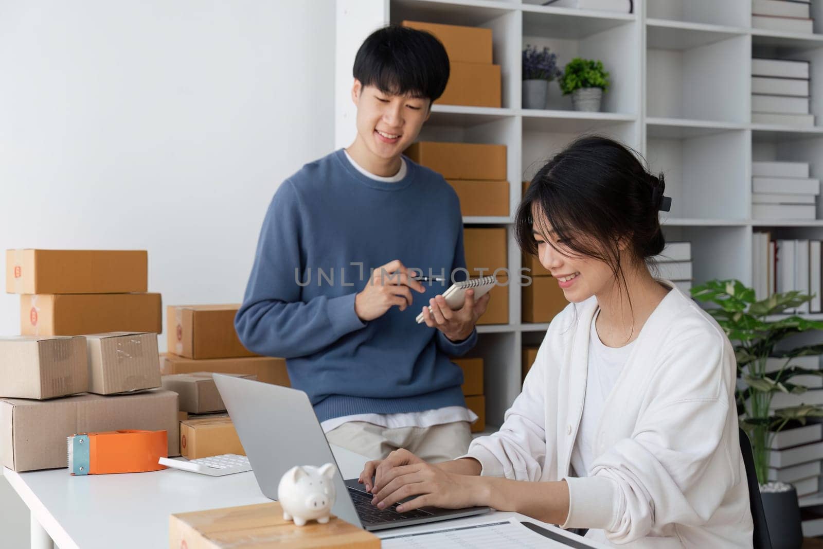 Couple of asian teenager owner business people work at home for online shopping, checking the order of product in technology computer and laptop, entrepreneur and life style concept.