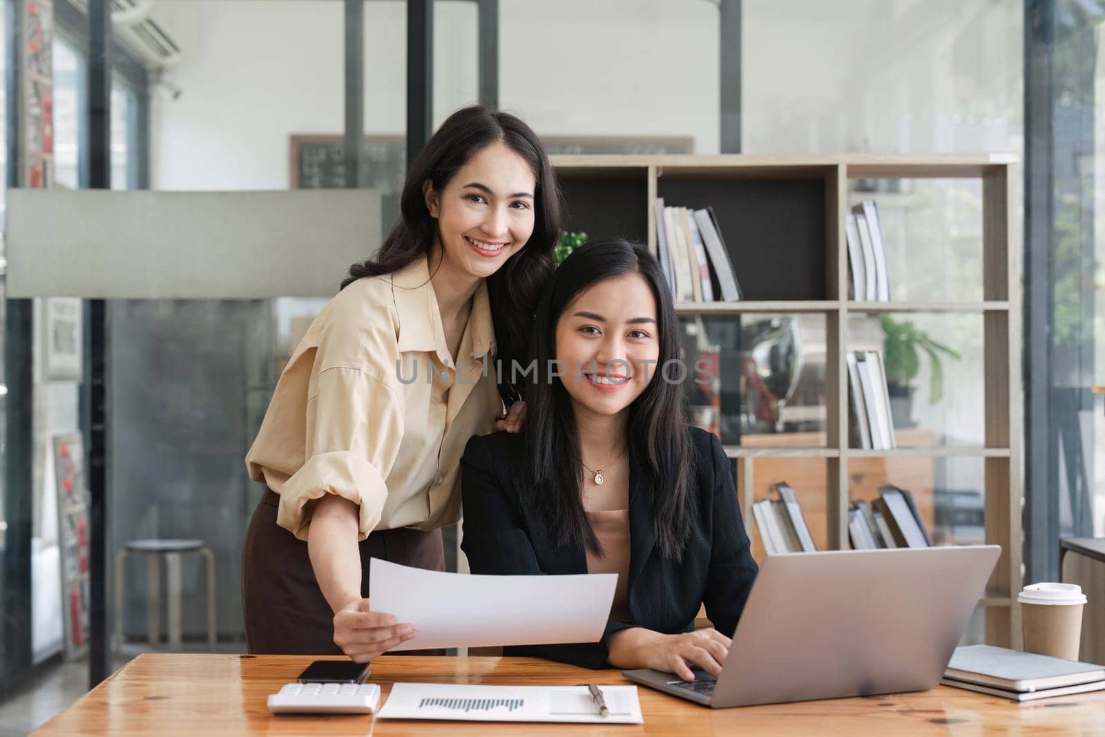 Two young businesswoman meeting and discussing about new business project plan, using computer analyzing financial and marketing with happiness at office.