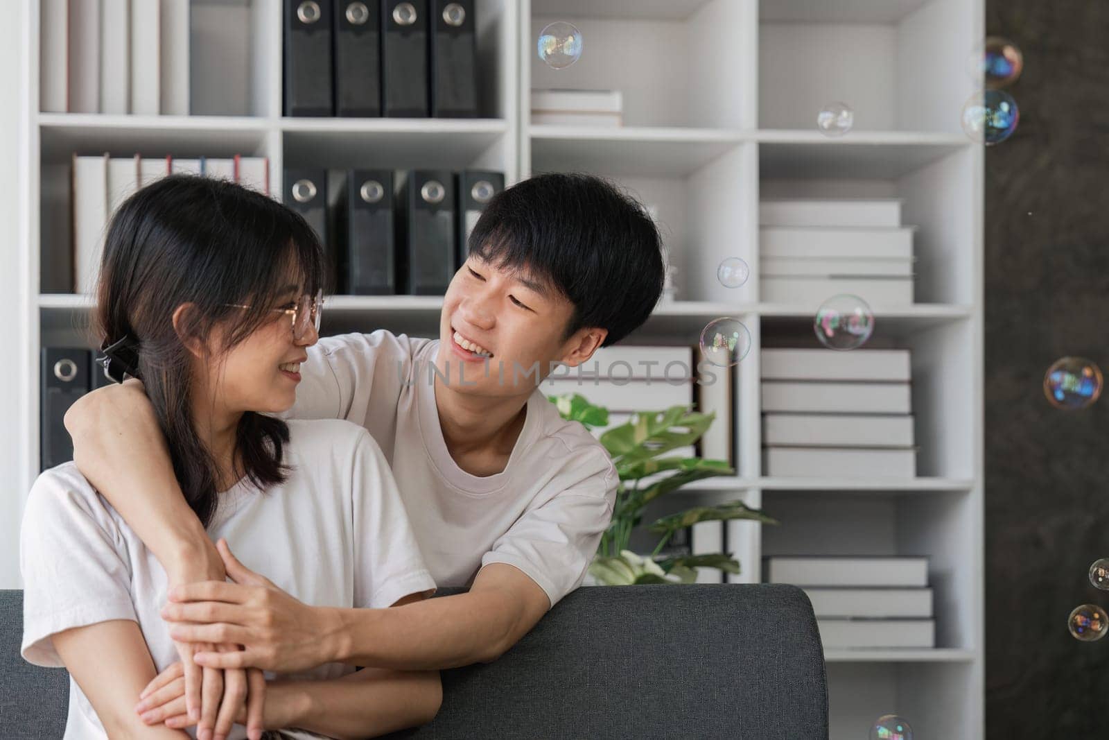 Smiling young couple embracing at office. Smiling man embracing from behind her happy girlfriend.