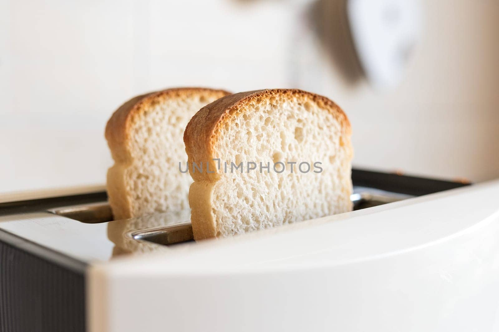 2 white fresh slices of bread in a white toaster, selective soft focus.