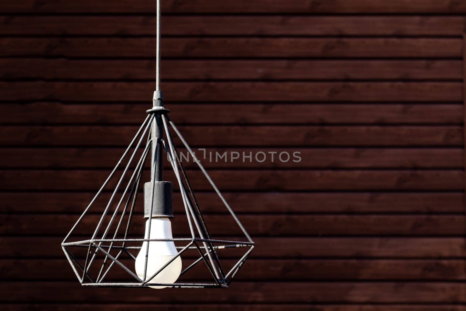 Close-up of modern pendant lamp hanging during on wooden wall background, copy space.