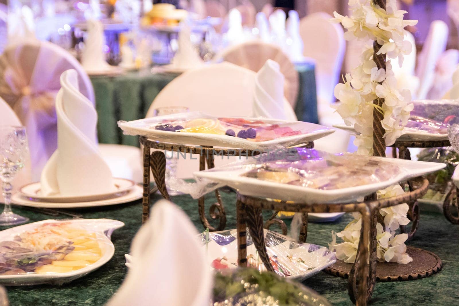 Serving a festive table on a green tablecloth before the arrival of guests in the banquet hall.