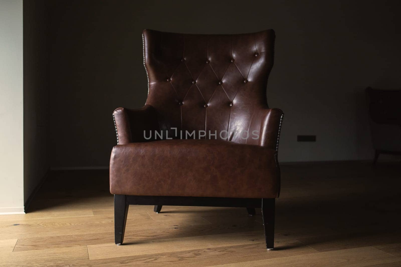 Brown leather armchair in an empty dark room by the window.