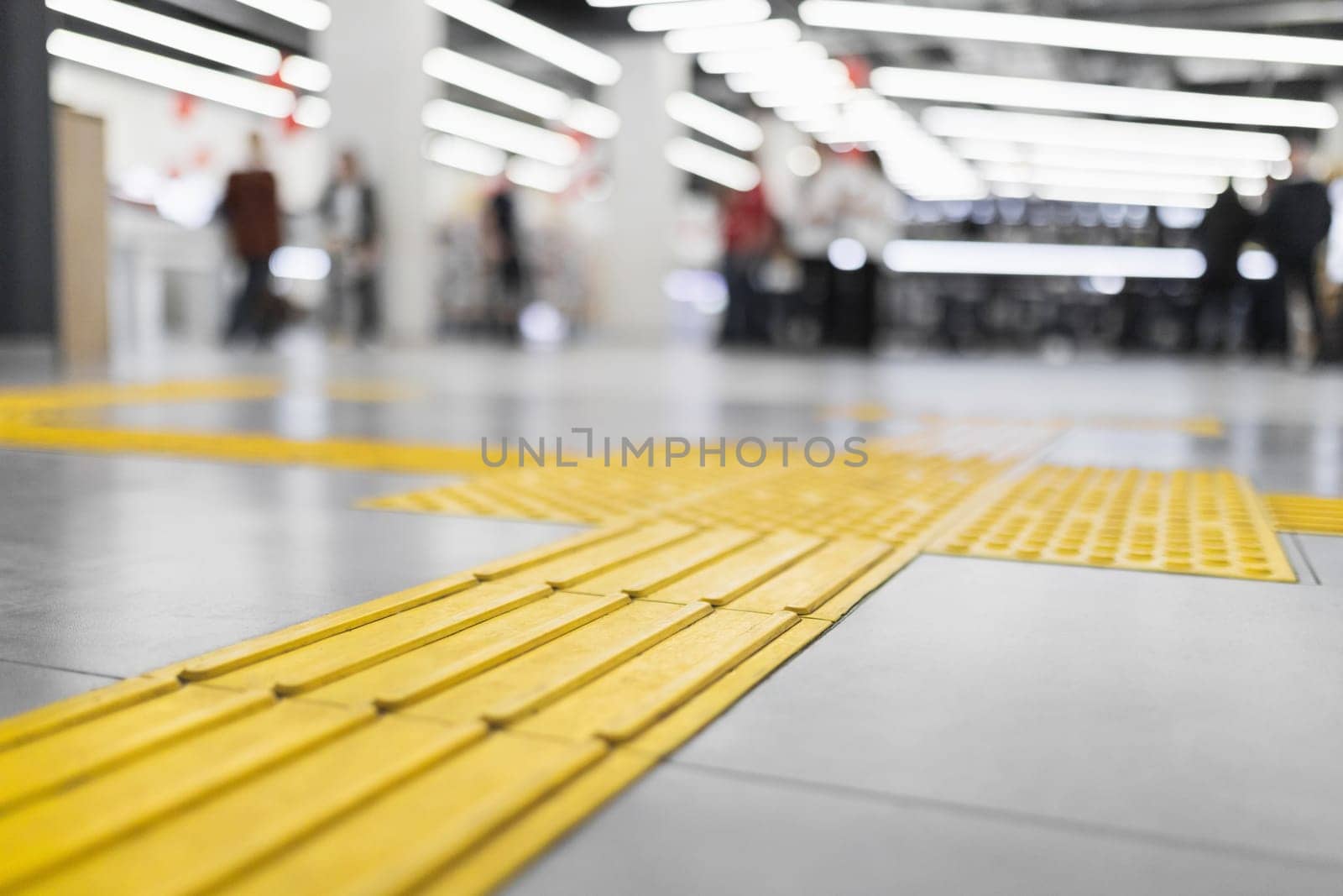 Yellow tactile tiles for the blind laid on a tiled floor in a store interior.