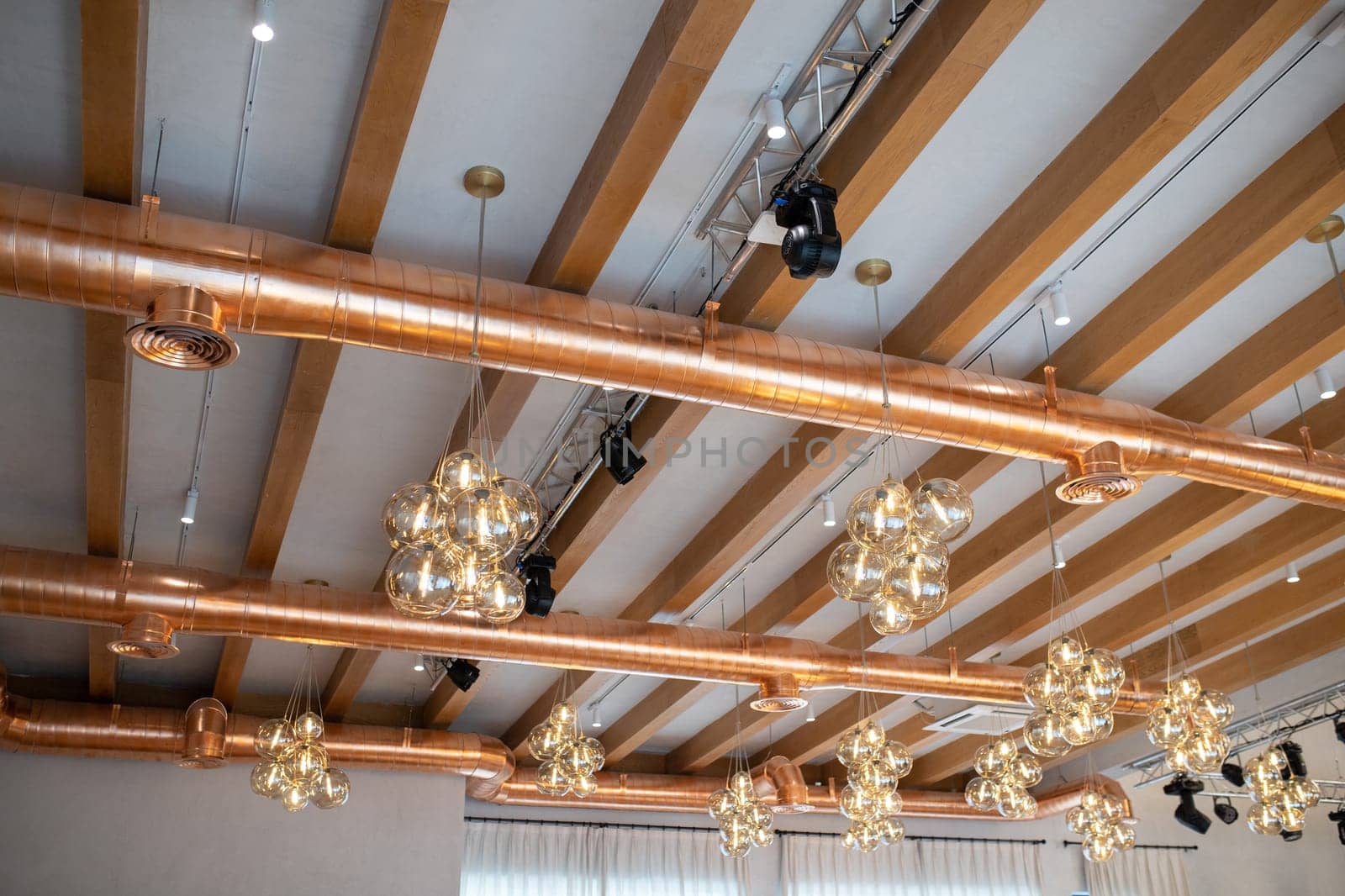 Ceiling in a modern loft style with wooden beams, ventilation, trusses and lighting.