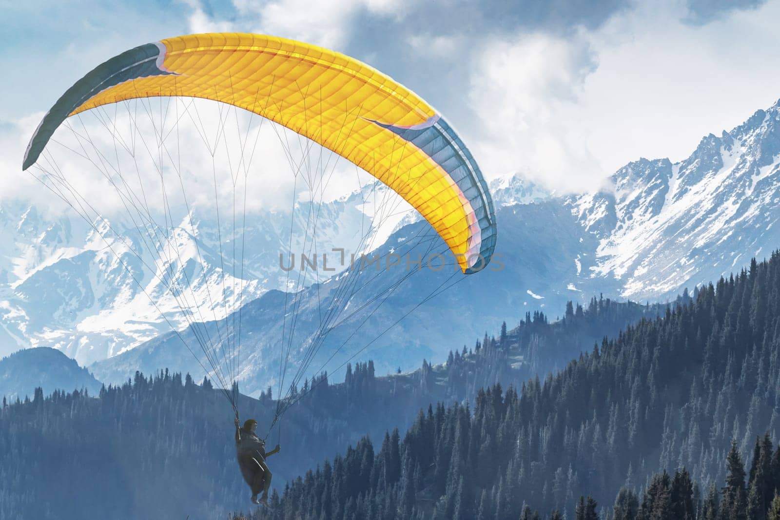 A paraglider flies against the backdrop of picturesque snow-capped mountains.