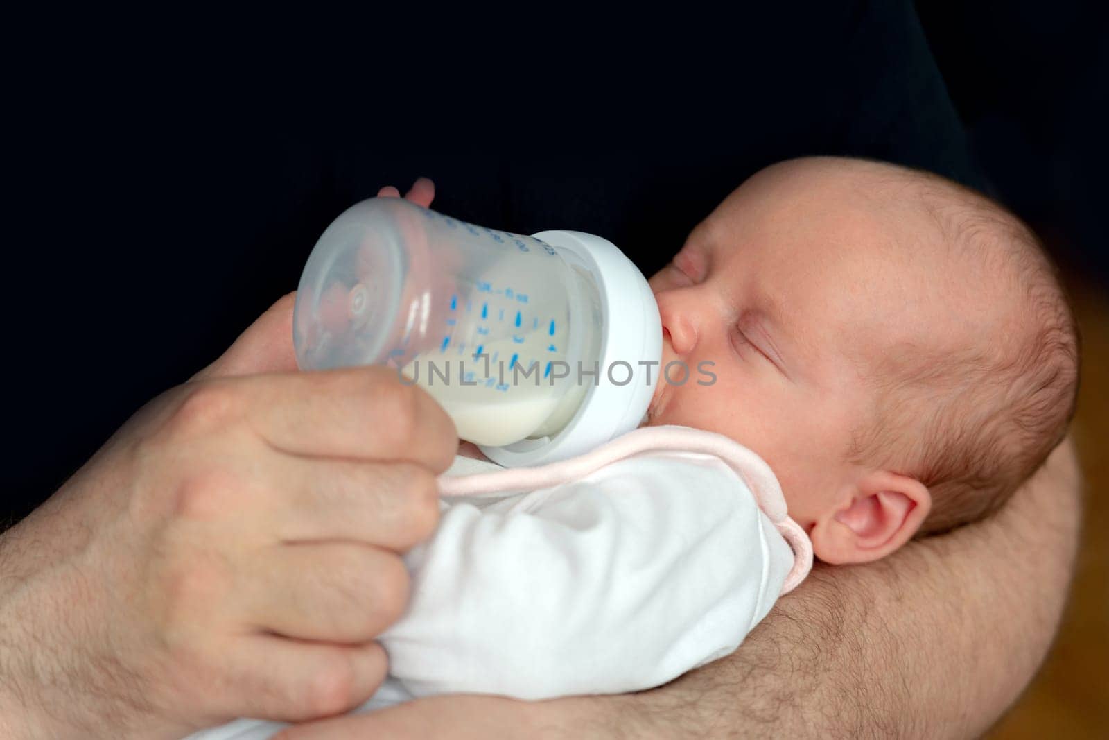 Little newborn baby eats milk formula from a bottle.