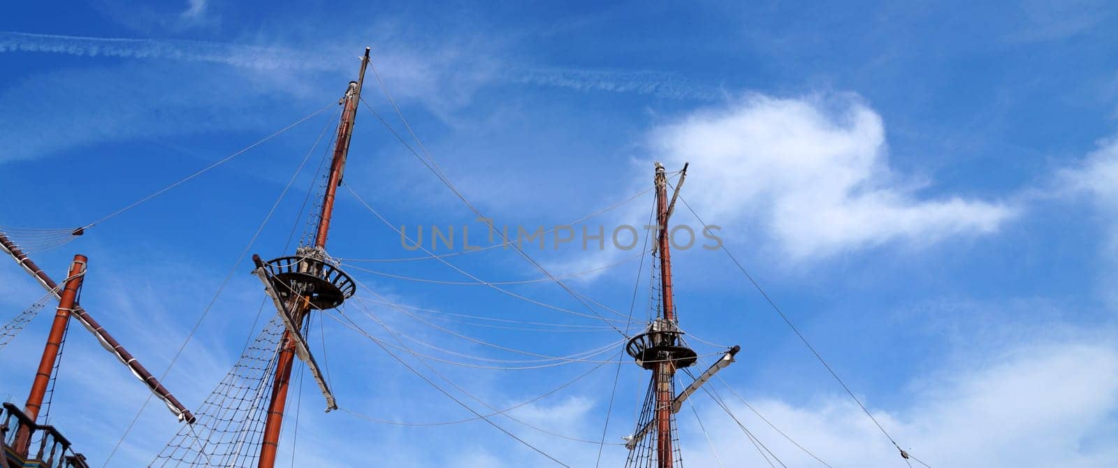 Masts of an old sea vessel without sails against a blue sunny sky, copy space by Annado