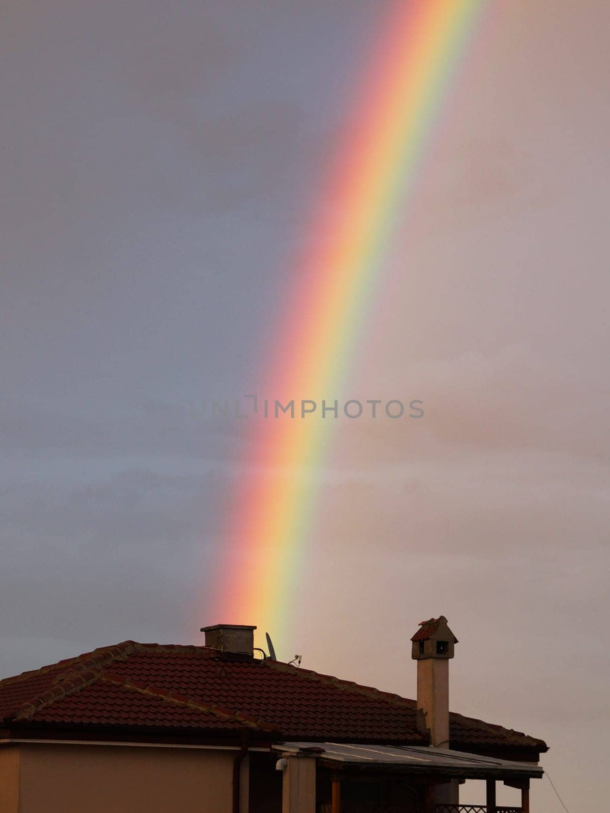 Multicolored rainbow in the sky after the rain over the roof of the house close-up