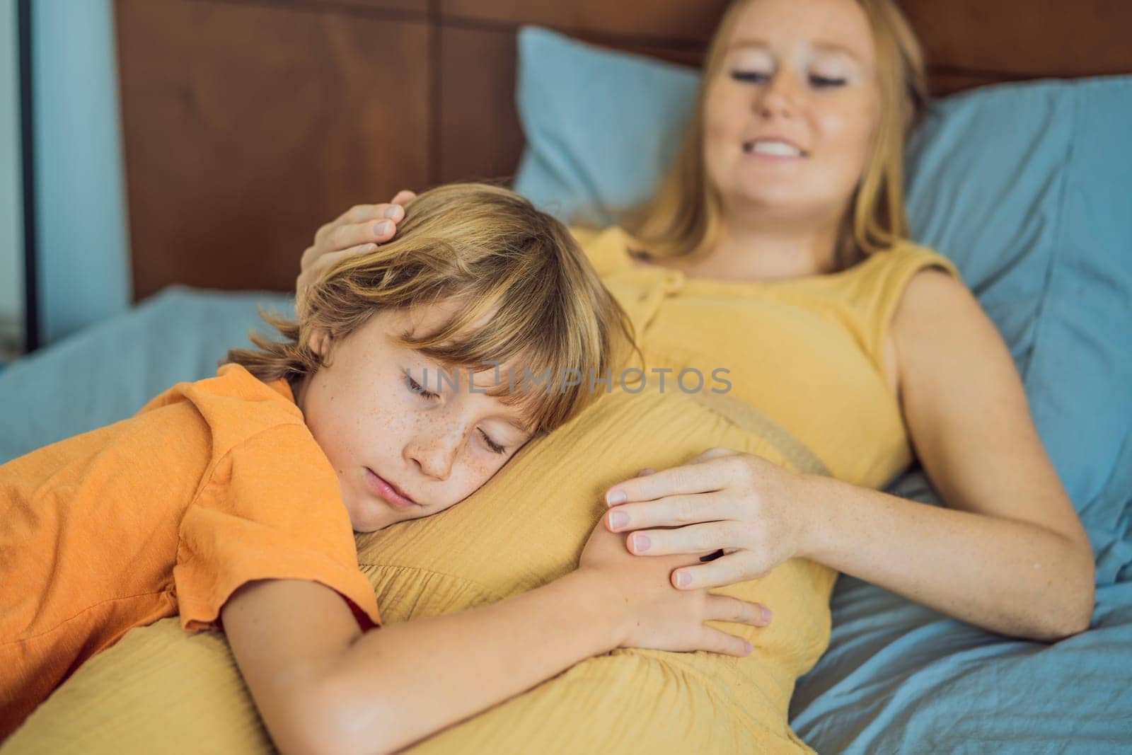 Young pregnant mother hugging her little boy lying in bed at night. Caring and loving parent hugging child.