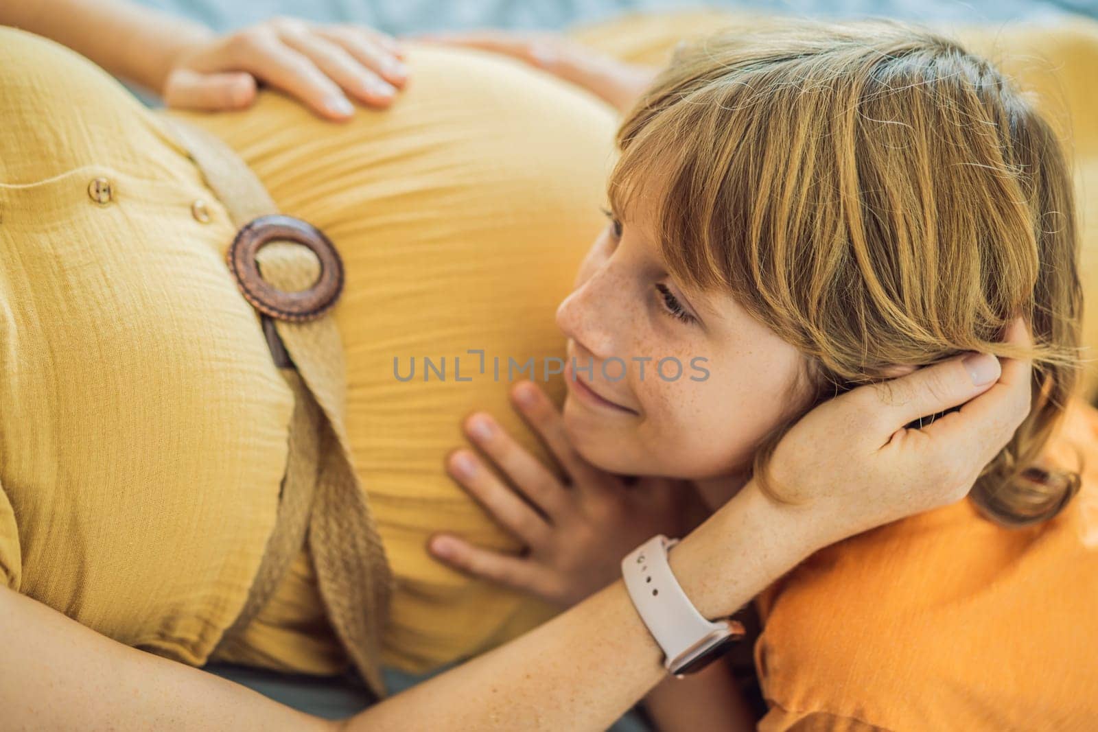 Young pregnant mother hugging her little boy lying in bed at night. Caring and loving parent hugging child.