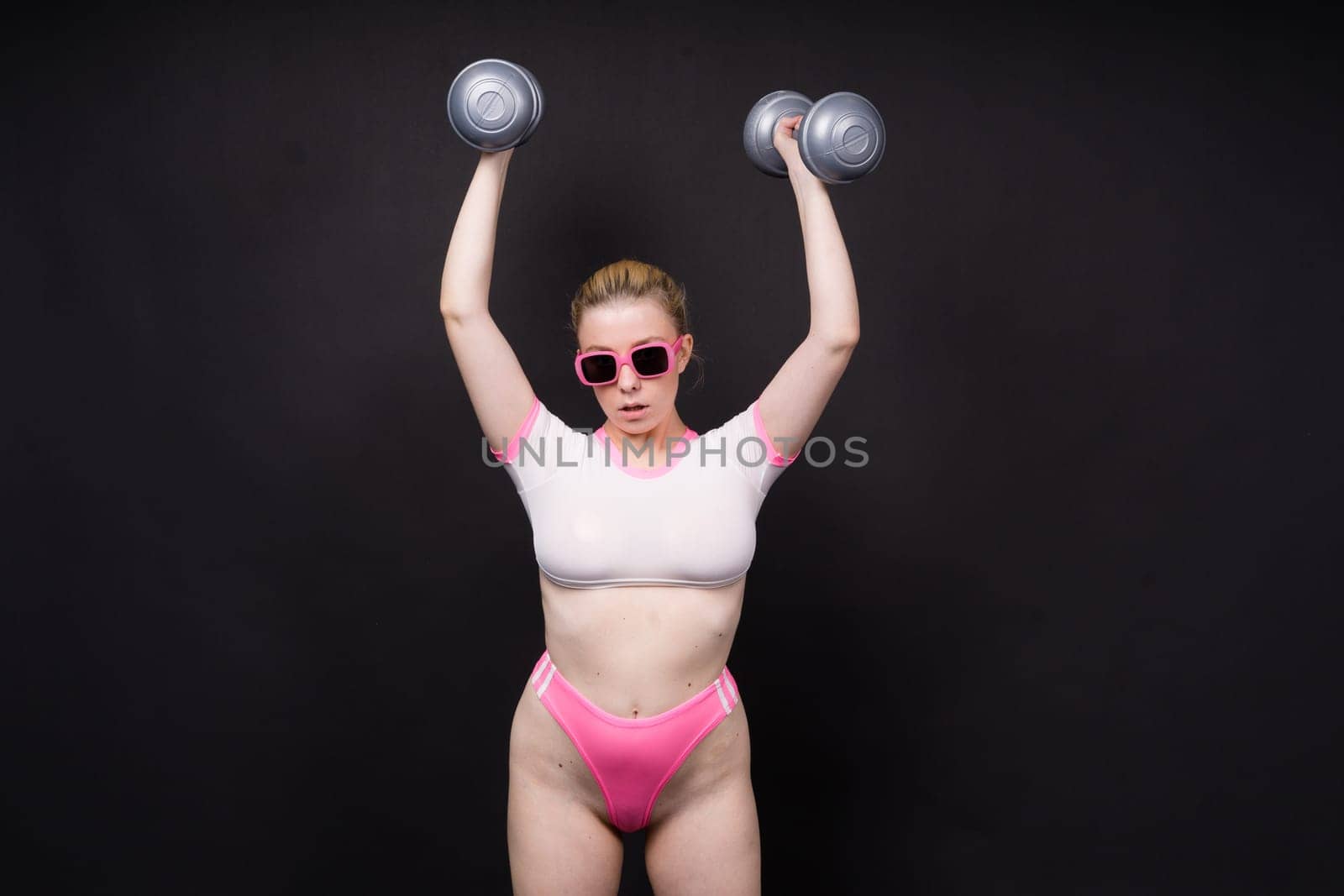 Seductive beautiful fitness female, athletic woman working out with dumbbells. Isolated in a studio