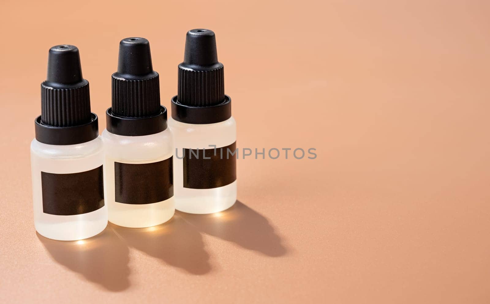 Set of plastic dropper bottles with liquid with black blank stickers. Mockup on brown background with shadow, copy space
