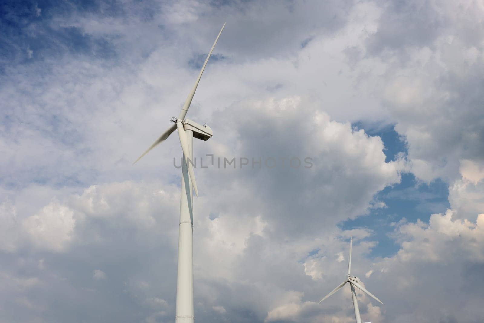 Two windmills of the power station against a cloudy sky view from below.