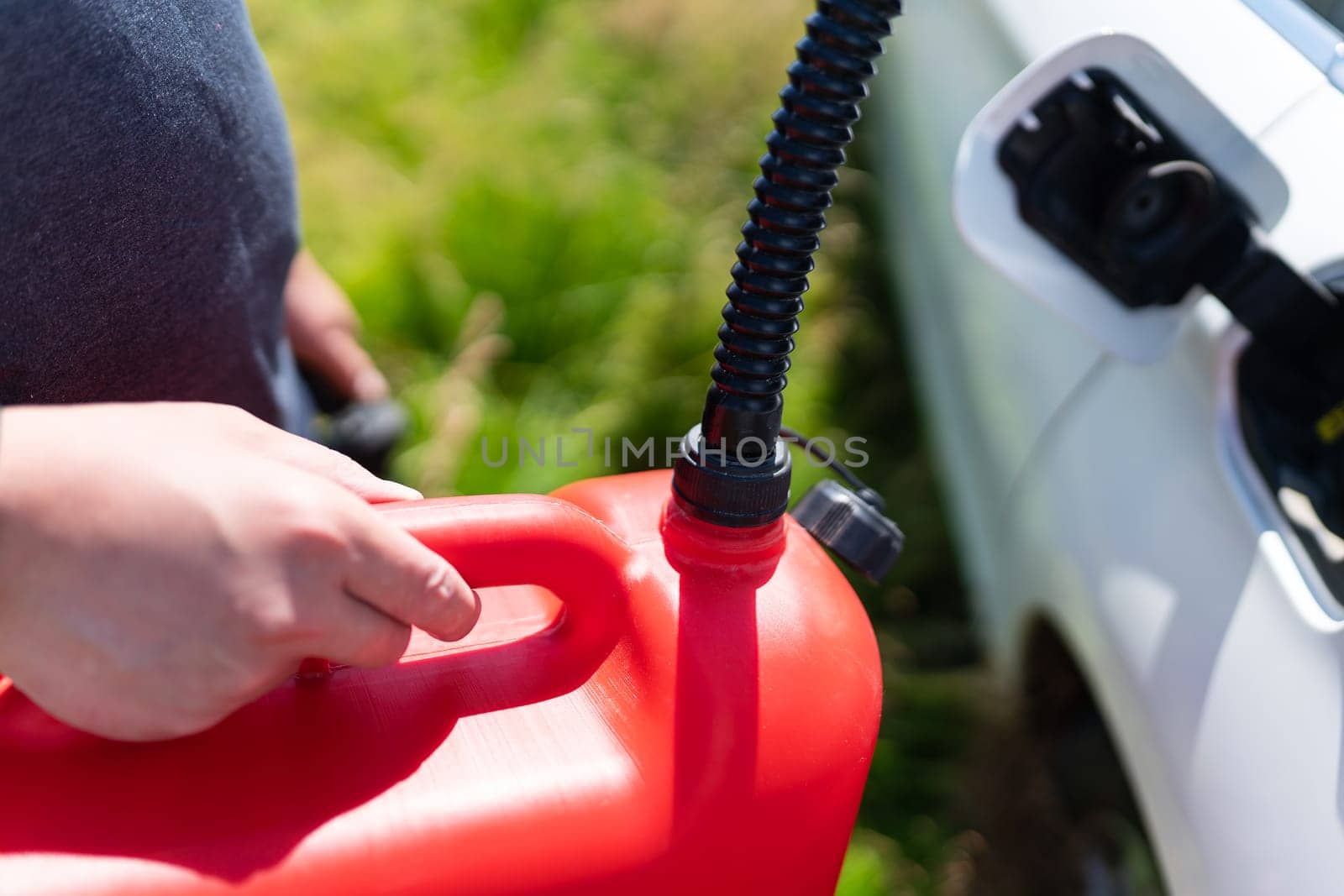 The driver fills up the empty tank of the car from a red canister on the side of the road. Fuel problem, force majeure. by sfinks