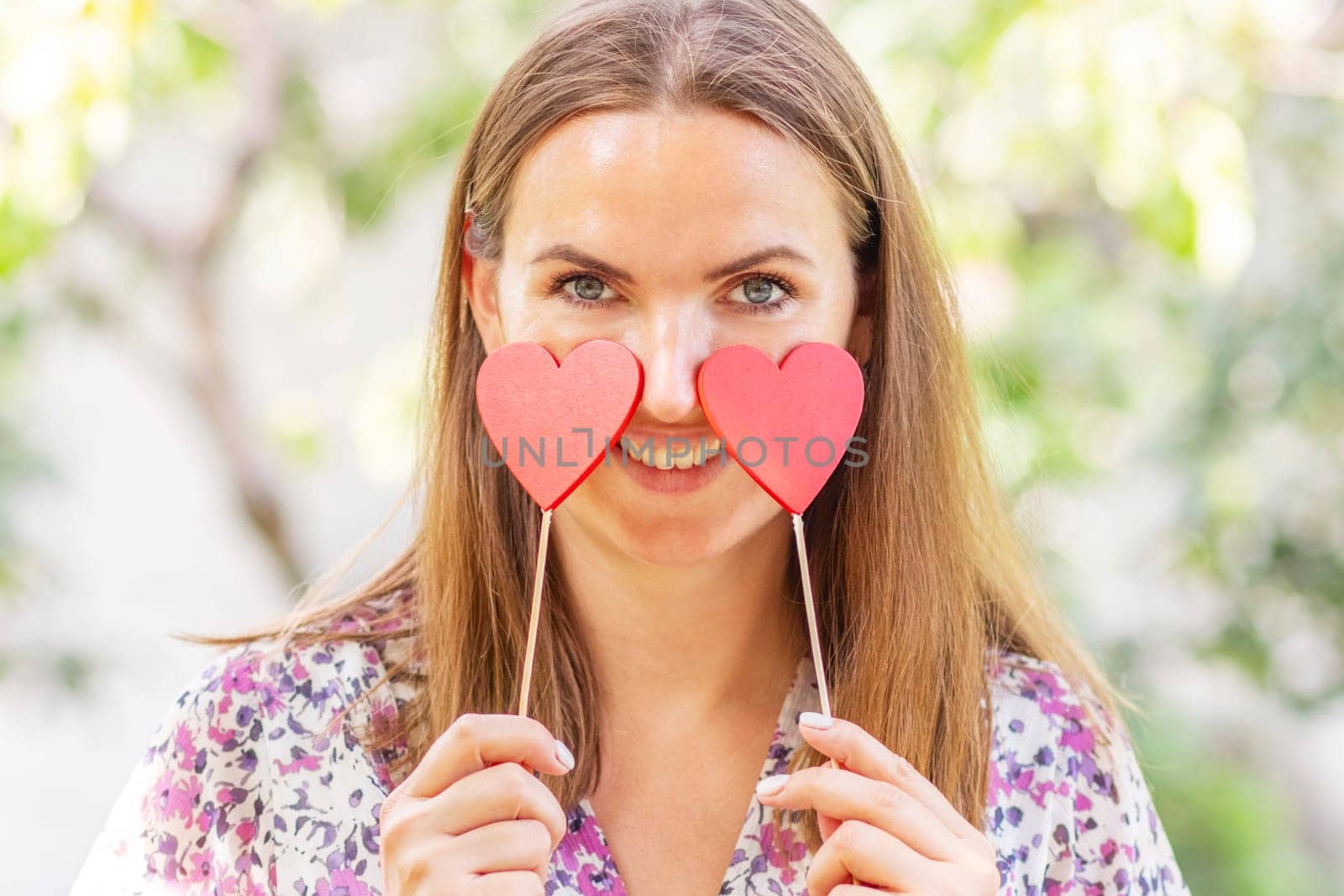 Happy beautiful woman with two decorative hearts in her hands is smiling on the natural backround.