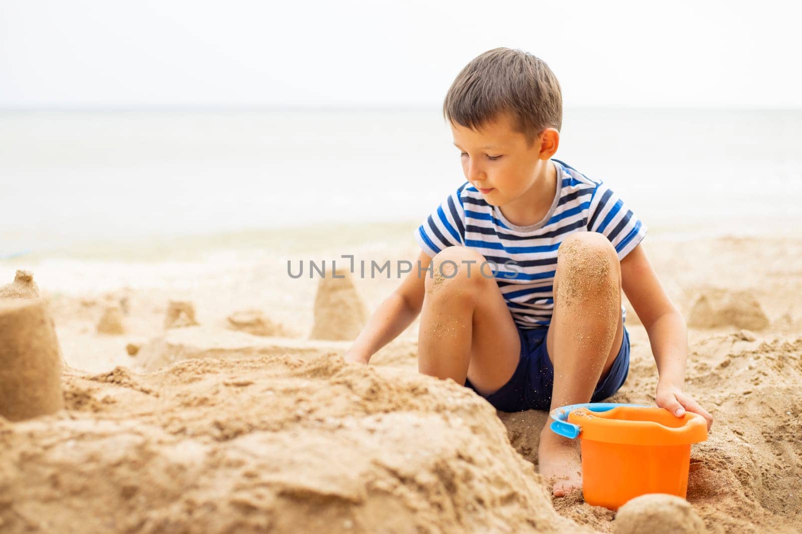Child playing with sand on beach in summer. Boy builds a sand castle on the sea by andreyz