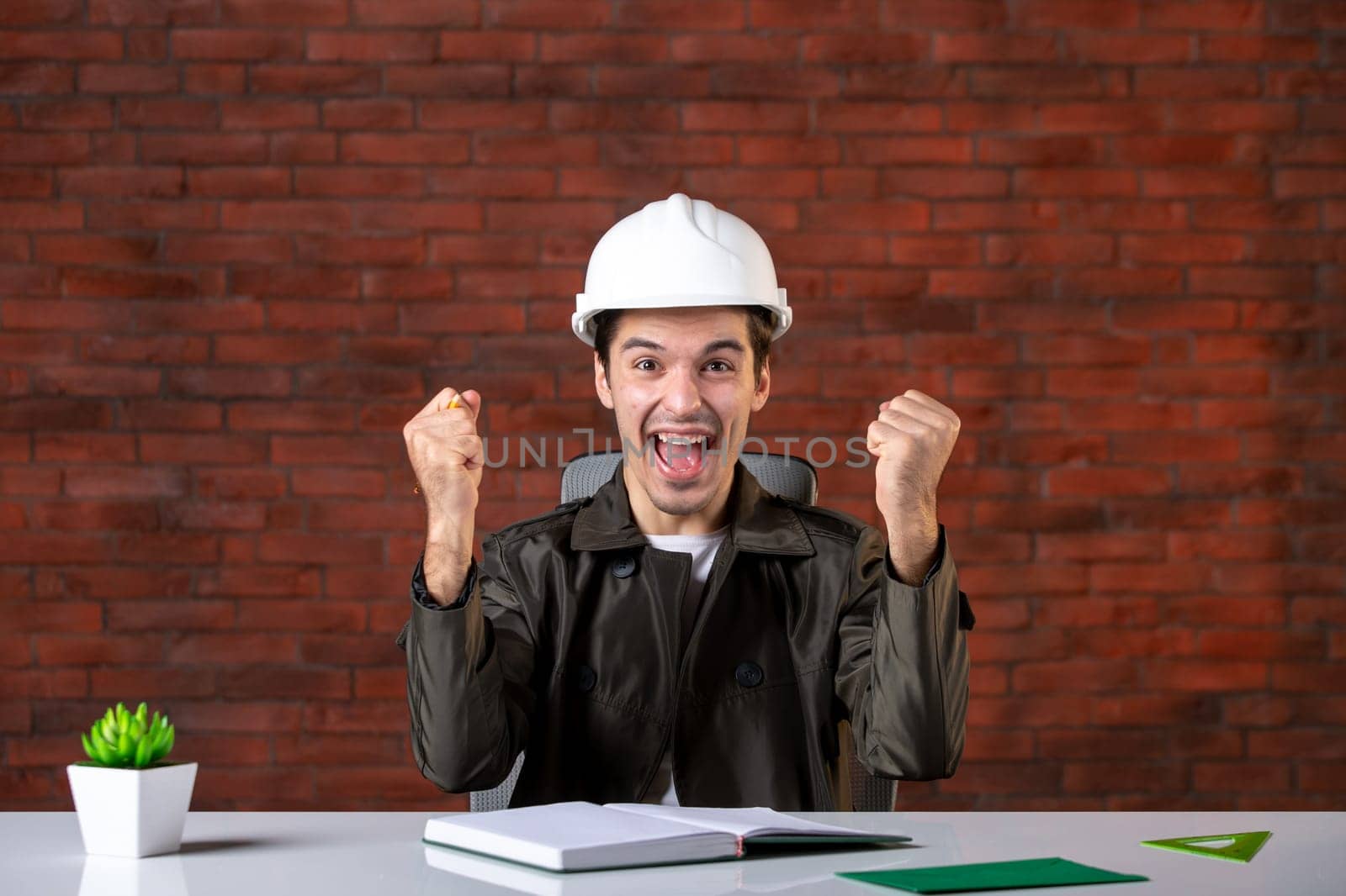 front view emotional male engineer sitting behind his working place and writing notes document plan business contractor property agenda builder corporate job