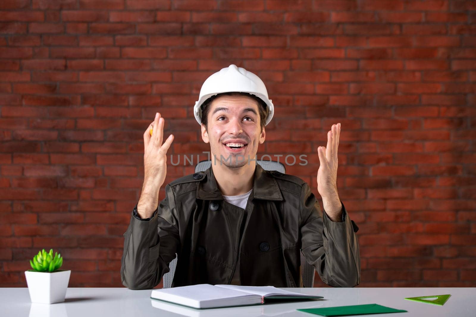 front view excited male engineer sitting behind his working place and writing notes document plan business contractor agenda builder corporate job property