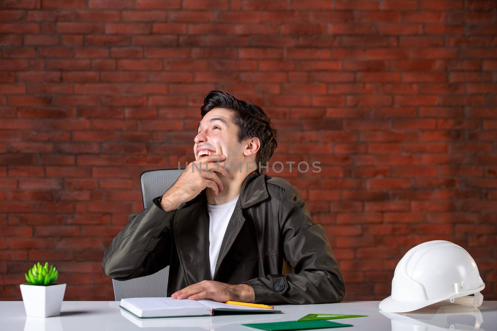 front view laughing male engineer sitting behind his working place job contractor agenda corporate business builder property document plan by Kamran