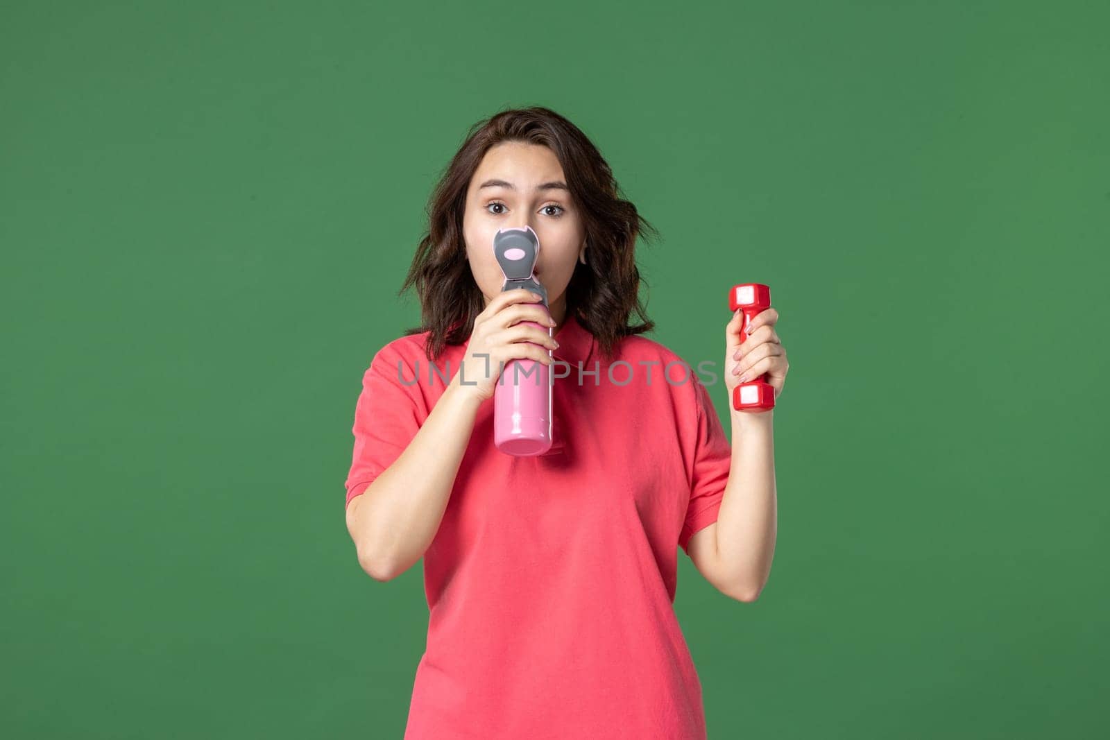 front view young saleswoman drinking from thermos and holding dumbbell on green background job color yoga uniform athlete shopping workout body work by Kamran