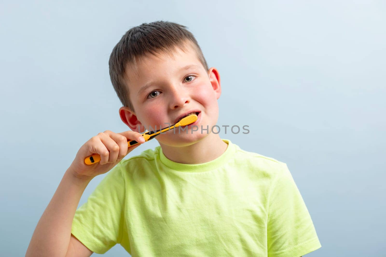 A child in t-shirt brushing teeth with toothbrush on blue background by andreyz