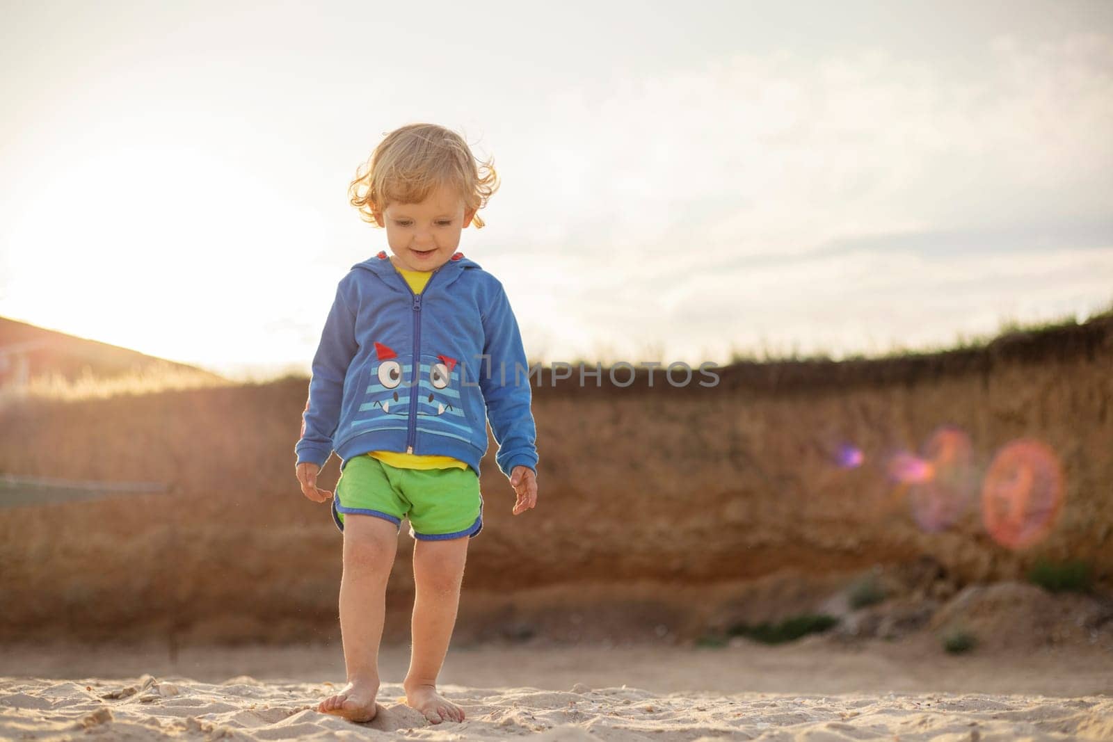 Happy child boy is walking on the beach at sunset. Cute blonde boy on a beach holiday.