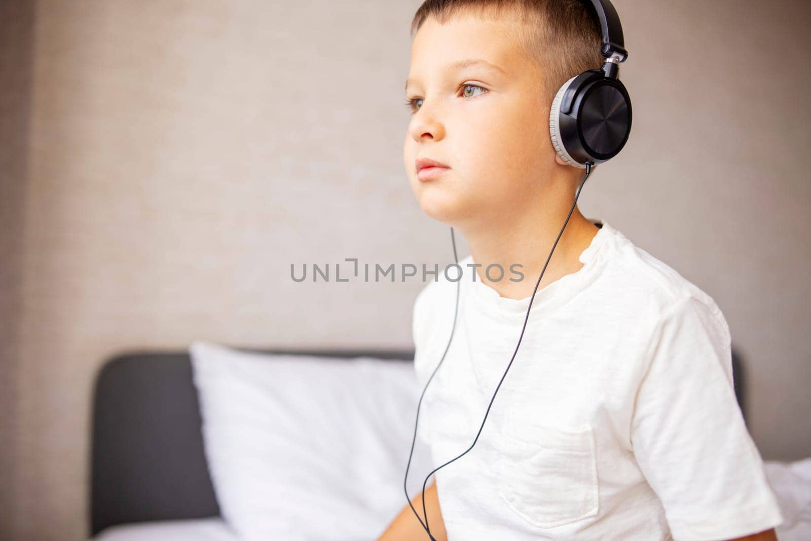 A boy in white T-shirt on bed playing with pc tablet and listening to music by andreyz
