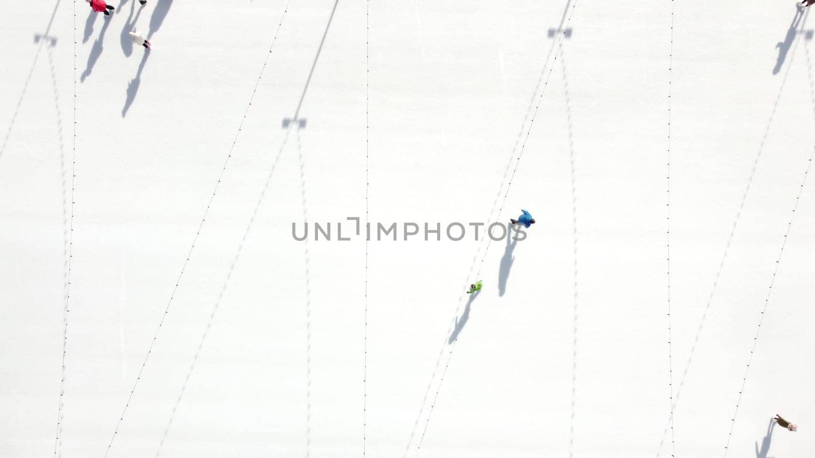 People ride on white ice rink on street and cast long shadows. People skating on sunny winter day. Top view. Aerial drone view. Leisure entertainment vacation weekend holidays activities lifestyle.