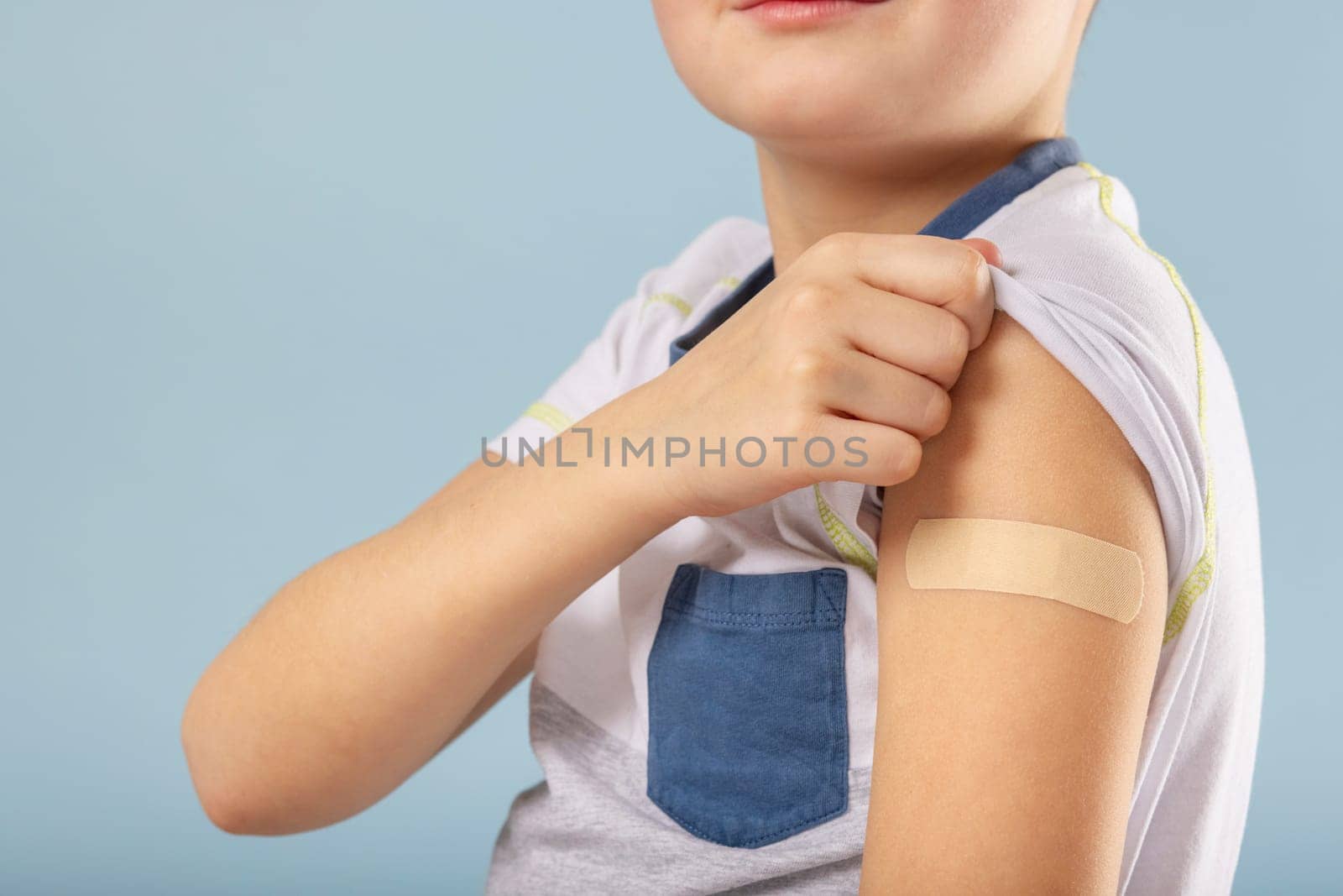 Vaccination of children. Vaccinated kid boy showing arm with adhesive bandage after vaccine injection. Kids and covid-19 prevention, antiviral immunization.