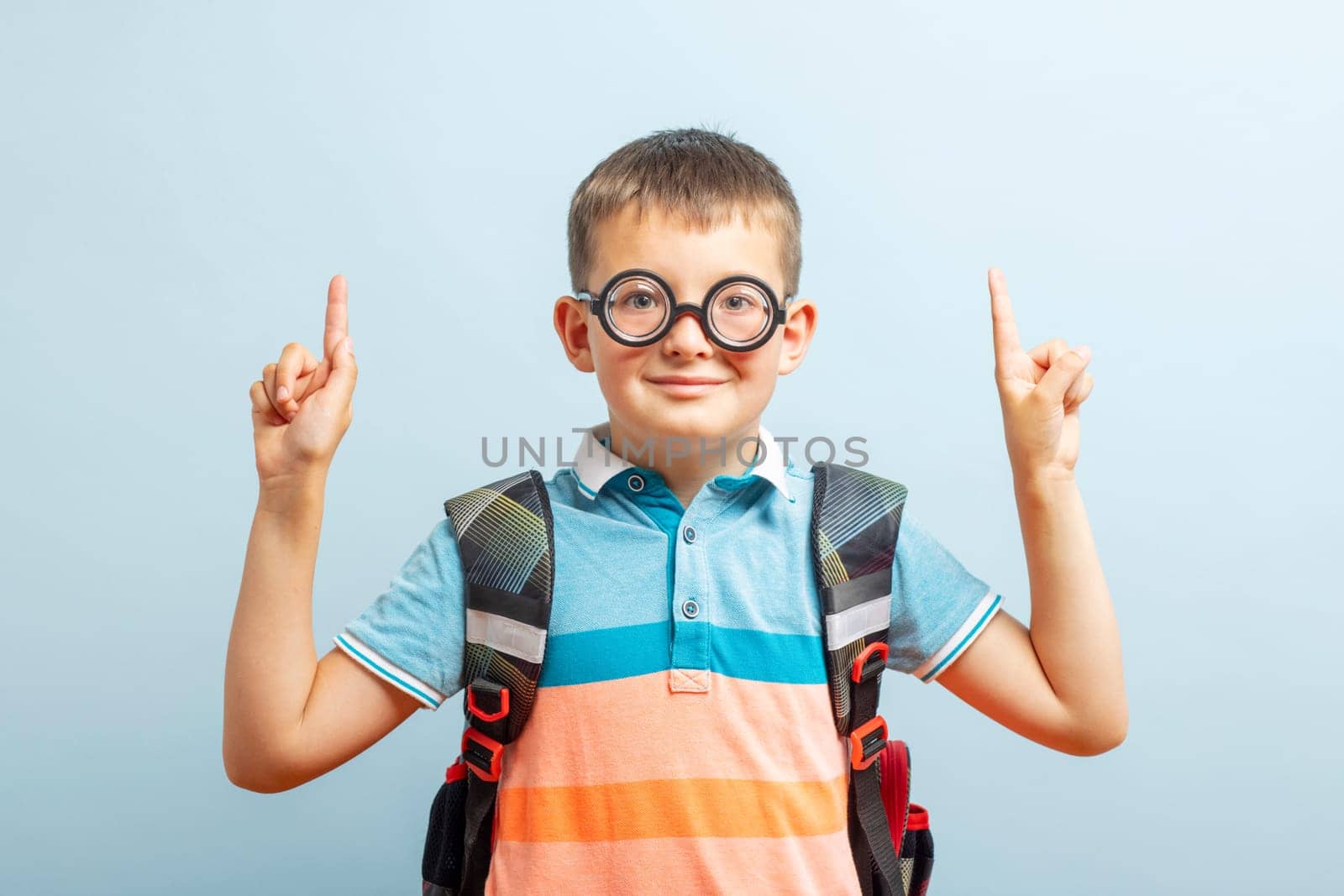 Happy school boy pointing fingers up showing something on blue background in studio. Free space for your text. Back to school.