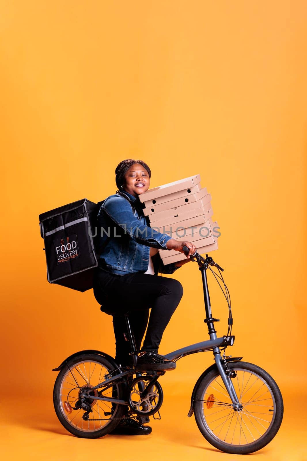 Restaurant worker riding bike while carrying stack of pizza delivering takeaway food meal by DCStudio