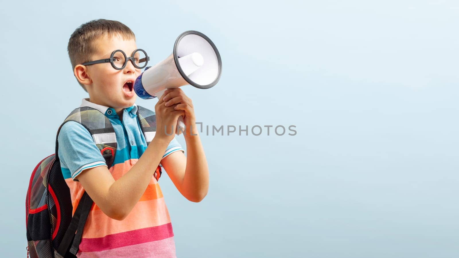 Little schoolboy with megaphone on blue background. Boy with megaphone making an announcement with copy space.